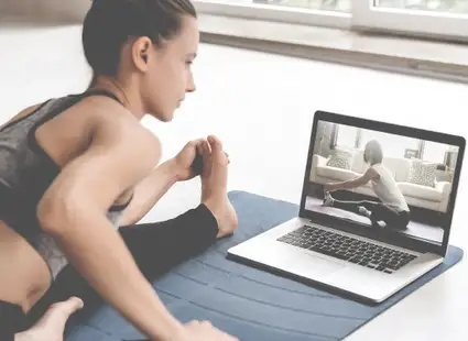 Eine junge Frau macht in ihrer Wohnung auf der Yogamatte Yoga vor ihrem Laptop