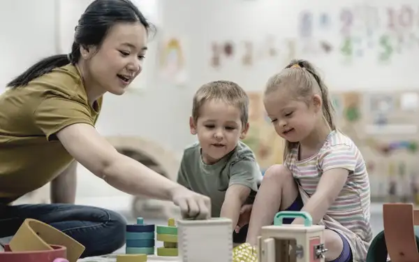 Eine Frau, die ein Masterstudium in Heilpädagogik absolviert, spielt mit zwei Kindern.