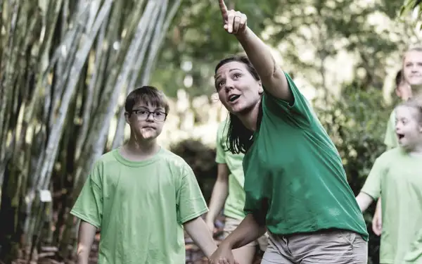 Eine Behindertenpädagogin zeigt einer Gruppe von Kindern mit Beeinträchtigung im Wald etwas Interessantes.