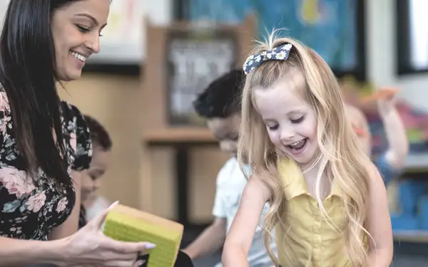 Eine duale Studentin, die Sozialpädagogik studiert, spielt fröhlich mit einem lächelnden Mädchen in einem Kindergarten.