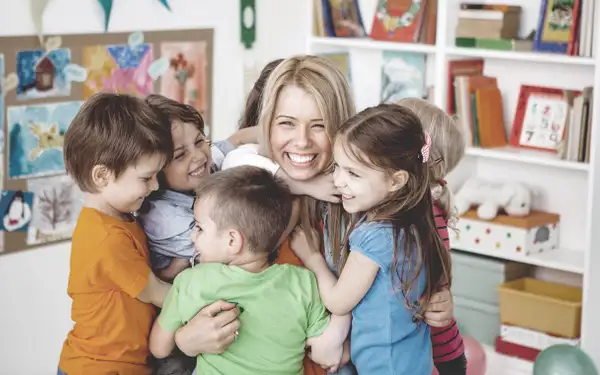 Sozialpädagogin umarmt Gruppe Kinder im Kindergarten.