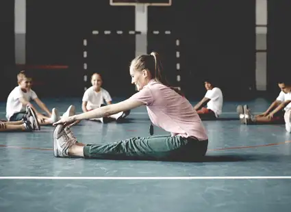 Eine Gesundheitspädagogin dehnt und streckt sich mit den Kindern in einer Turnhalle.