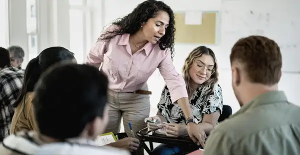 Eine Frau, die ein Fernstudium in Pädagogik absolviert, hilft mehreren erwachsenen Schülern in einem Klassenzimmer.