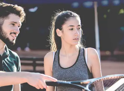 Spielerberater spricht mit junger Sportlerin auf einem Tennisplatz.