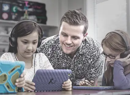 Ein Bildungswissenschaftler lernt mit Kindern, die ein Tablet in der Hand halten. 