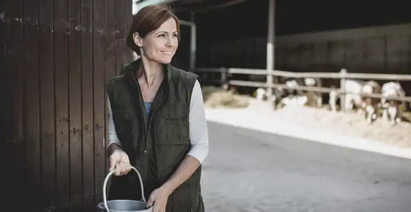 Eine Landwirtin, die Agrarwirtschaft studiert hat, steht mit einem Eimer in der Hand auf ihrem Bauernhof.