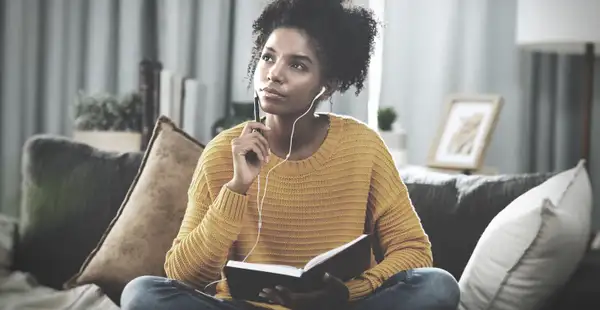 Eine junge Frau sitzt auf der Couch und hält einen Stift und ein Notizbuch. Sie überlegt sich Formulierungen für ihr Motivationsschreiben für das Wirtschaftspsychologie Studium.