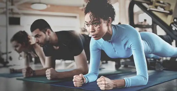 Fitnesstrainer*innen machen einen Unterarmstütz auf ihren Matten im Fitnessstudio.