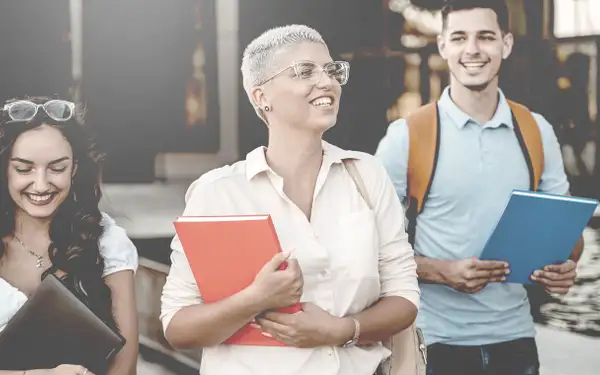 Drei Studierende laufen über den Campus. In der Hand halten sie Unterlagen.