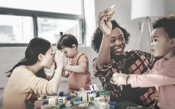 Zwei Frühpädagoginnen spielen mit zwei Kleinkindern. 