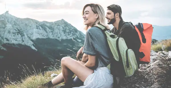 Wanderer schauen von einem Berggipfel herab in die Landschaft.