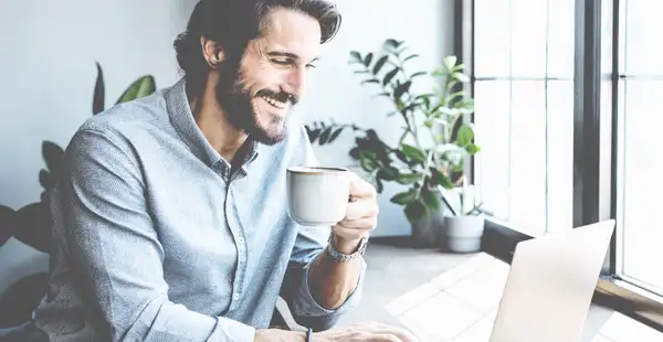 Junger Sportmanager sitzt in seinem Büro am Laptop und trinkt Kaffee.