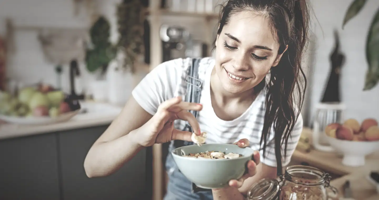 Eine Studentin des Fachbereichs Ernährung kocht. Sie hält eine Schüssel mit einem Gericht in der Hand und lächelt.