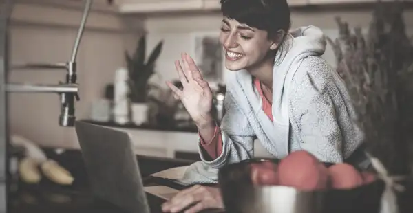 Eine Studentin des Fernstudiengangs Ernährungsberatung sitzt vor ihrem Laptop und winkt während einer Online-Vorlesung in die Kamera. 