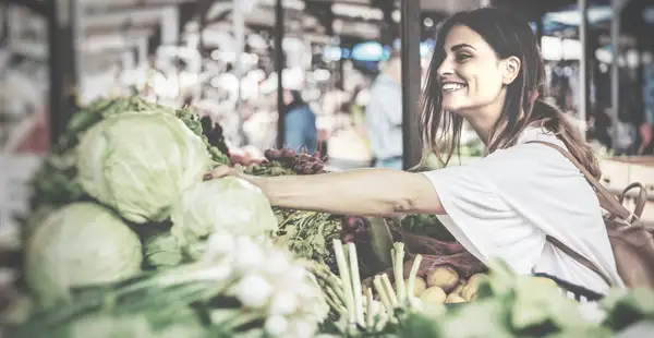 Eine Ernährungsberaterin in Ausbildung greift auf einem Markt nach Gemüse. 