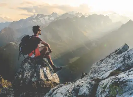 Ein Wanderer sitzt auf einem Berg und schaut in die Ferne.