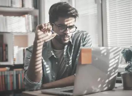 Ein Wirtschaftspsychologie Student sitzt an seinem Schreibtisch am Laptop und denkt über den Studienabbruch nach.