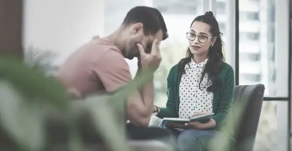 Eine Arbeitspsychologin unterhält sich mit einem Klienten, der das Gesicht in den Händen vergräbt.