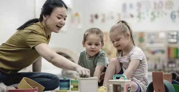 Eine Frau, die ein Masterstudium in Heilpädagogik absolviert, spielt mit zwei Kindern.