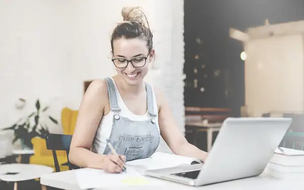 Eine junge Studentin macht sich auf ihrem Laptop Notizen für die Vorlesung.