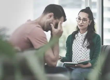 Eine Arbeitspsychologin unterhält sich mit einem Klienten, der das Gesicht in den Händen vergräbt.