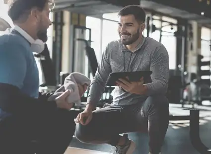 Ein Sportwissenschaftler berät einen Klienten im Fitnessstudio.