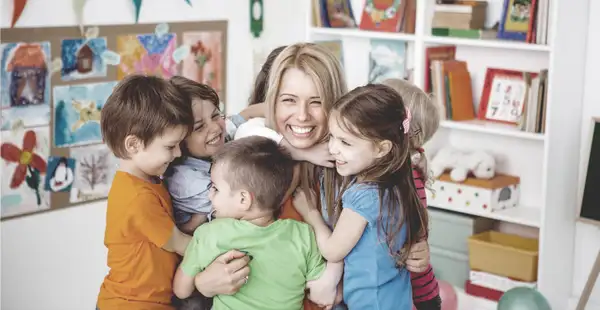 Sozialpädagogin umarmt Gruppe Kinder im Kindergarten.