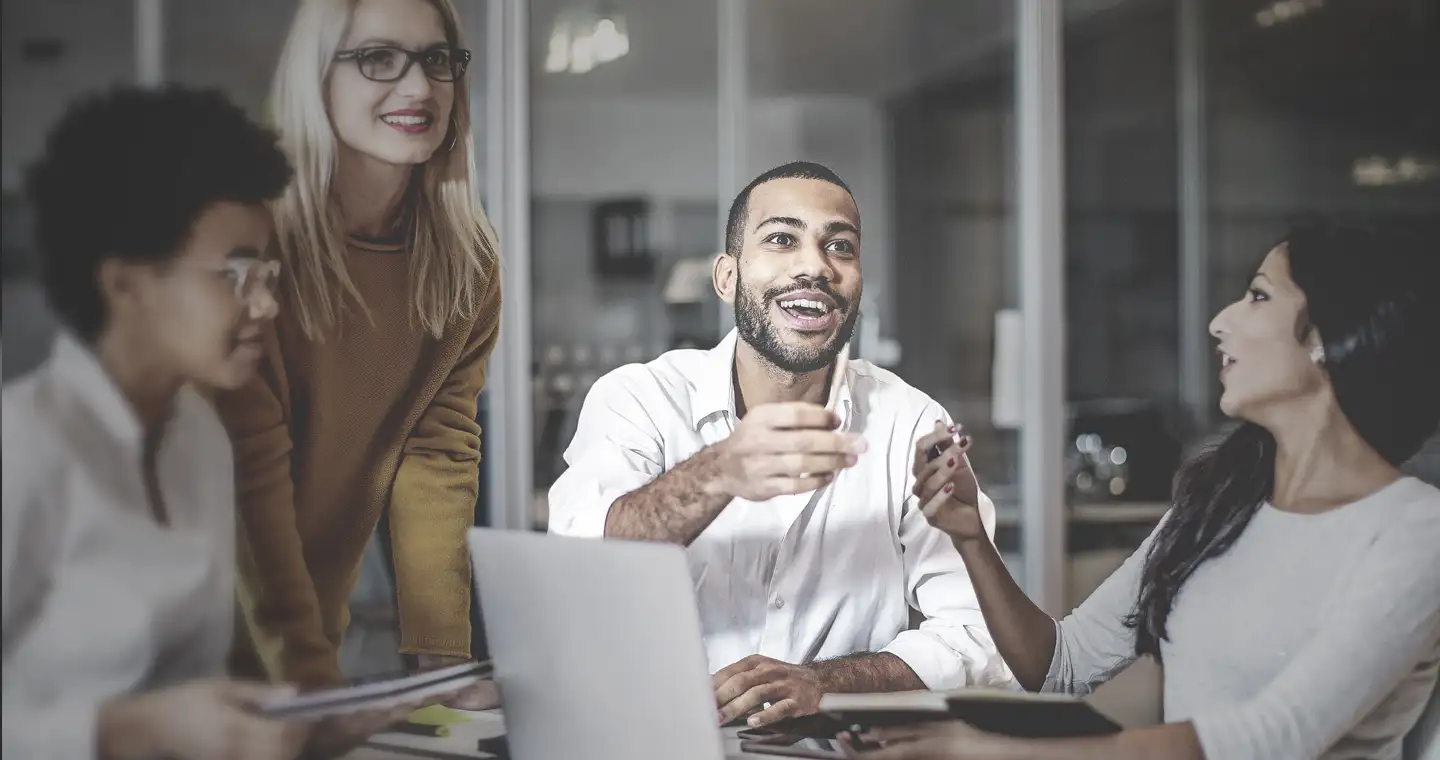 Vier Kolleg*innen aus dem Personalmanagement unterhalten sich angeregt im Büro und witzeln dabei zwischendurch.