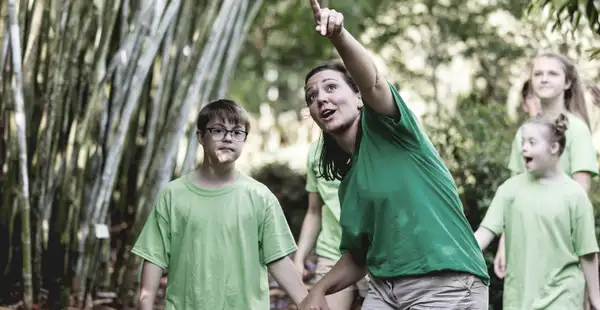 Eine Behindertenpädagogin zeigt einer Gruppe von Kindern mit Beeinträchtigung im Wald etwas Interessantes.