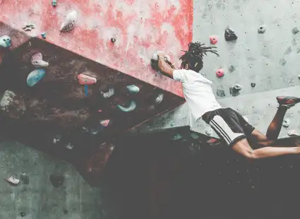 Ein sportlicher junger Mann in lässigen Sportklamotten lässt beim Bouldern an der Kletterwand seine Beine baumeln.