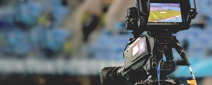 Eine professionelle Filmkamera filmt ein Fußballstadion.