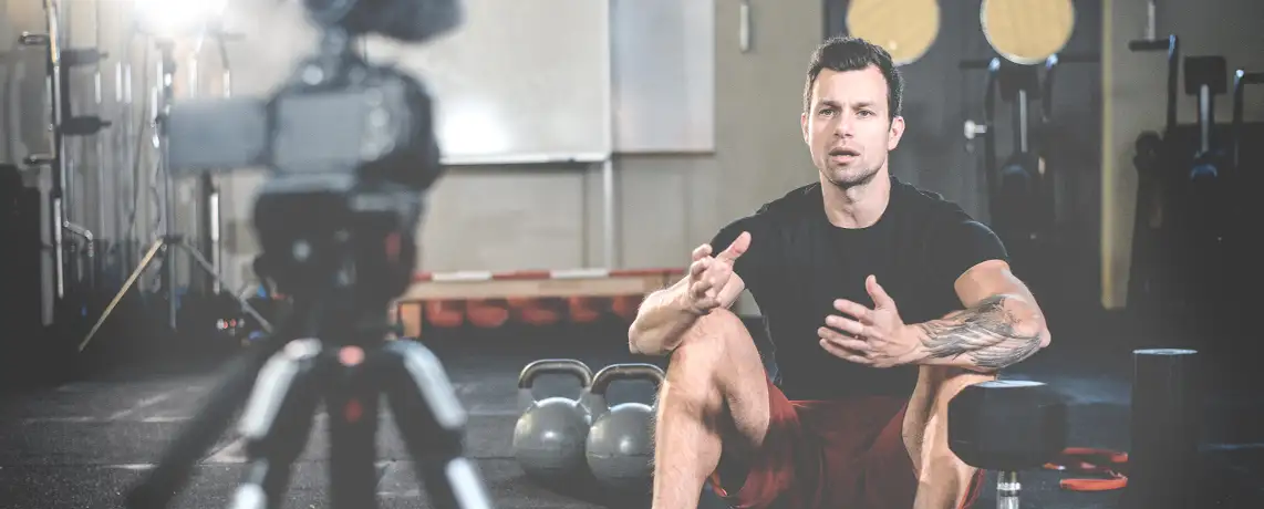 Junger Sportjournalist übt das Sprechen vor der Kamera im Fitnessstudio.