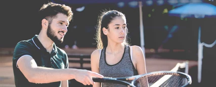 Spielerberater spricht mit junger Sportlerin auf einem Tennisplatz.