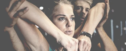 Junger Sportphysiotherapeut unterstützt eine junge Sportlerin bei einer Dehnübung für die Arme.