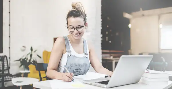 Eine Studentin macht sich Notizen, während sie an einer Online-Vorlesung teilnimmt.