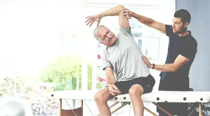 Junger Sporttherapeut behandelt einen älteren Patienten.