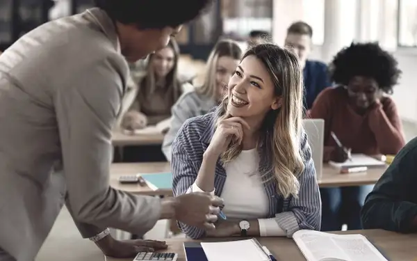 Eine Frau, die den Master in Bildungswissenschaften absolviert, sitzt lächelnd in einem Klassenzimmer und spricht mit einer Dozentin.