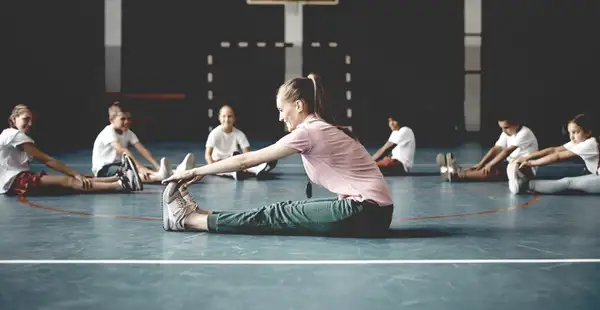 Eine Gesundheitspädagogin dehnt und streckt sich mit den Kindern in einer Turnhalle.