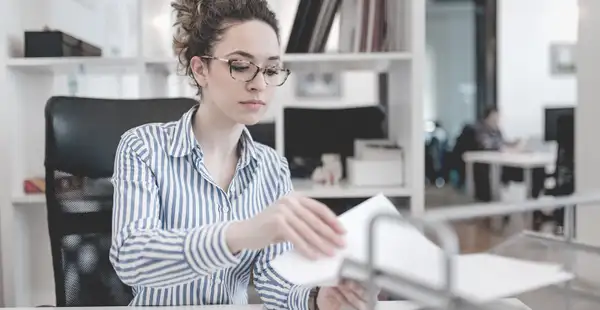 Eine Frau, die Bildungsmanagement studiert hat, arbeitet konzentriert in einem Büro und sortiert Dokumente.