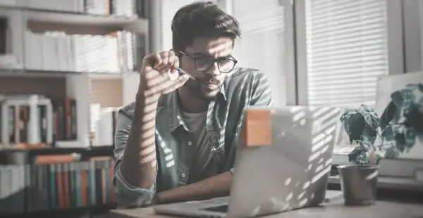 Ein Wirtschaftspsychologie Student sitzt an seinem Schreibtisch am Laptop und denkt über den Studienabbruch nach.