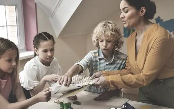 Eine Absolventin des Masterstudiengangs Erziehungswissenschaft bastelt mit drei Kindern.