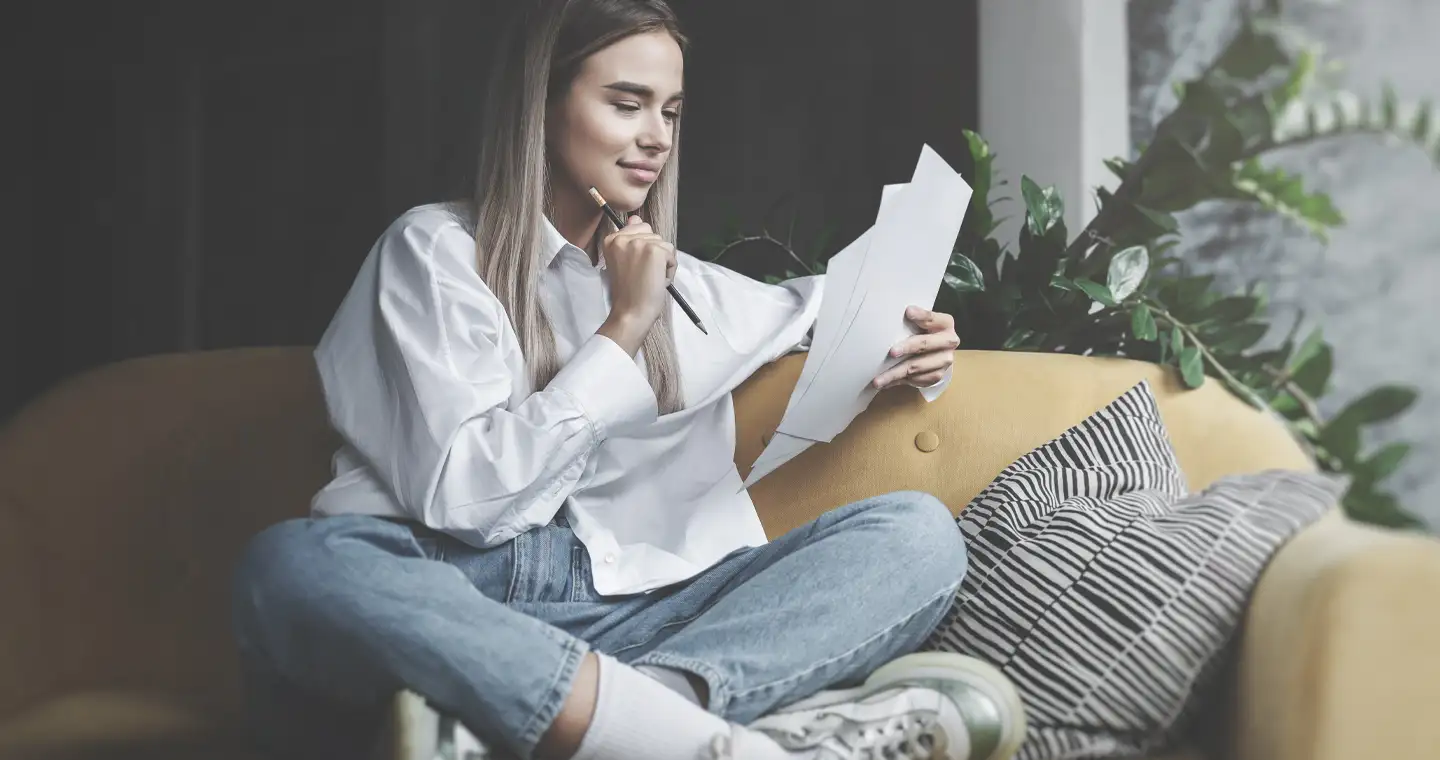 Eine Schulabsolventin sitzt auf der Couch und schreibt Stichpunkte für ein beispielhaftes Motivationsschreiben auf.