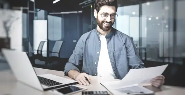 Ein Bilanzbuchhalter sitzt in einem Büro und begutachtet gutgelaunt ein Dokument zum Jahresabschluss.