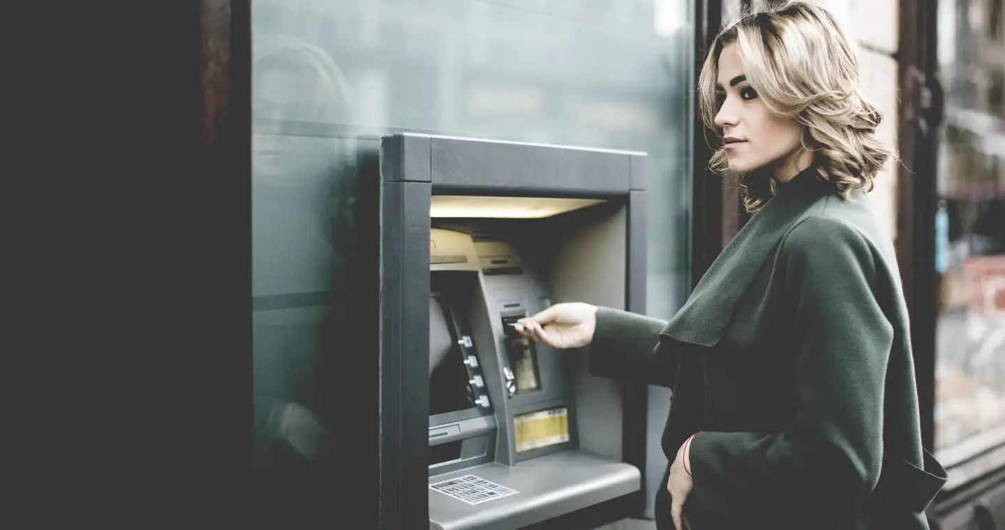 Junge Frau steht vor Bankautomat.