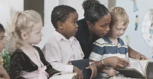 Eine Religionspädagogin liest einer Gruppe von Kindern aus der Bibel vor. Die Kinder hören aufmerksam zu.