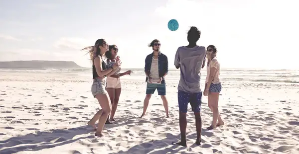 Junge Studierende spielen Volleyball am Strand.