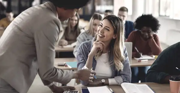 Eine Frau, die den Master in Bildungswissenschaften absolviert, sitzt lächelnd in einem Klassenzimmer und spricht mit einer Dozentin.